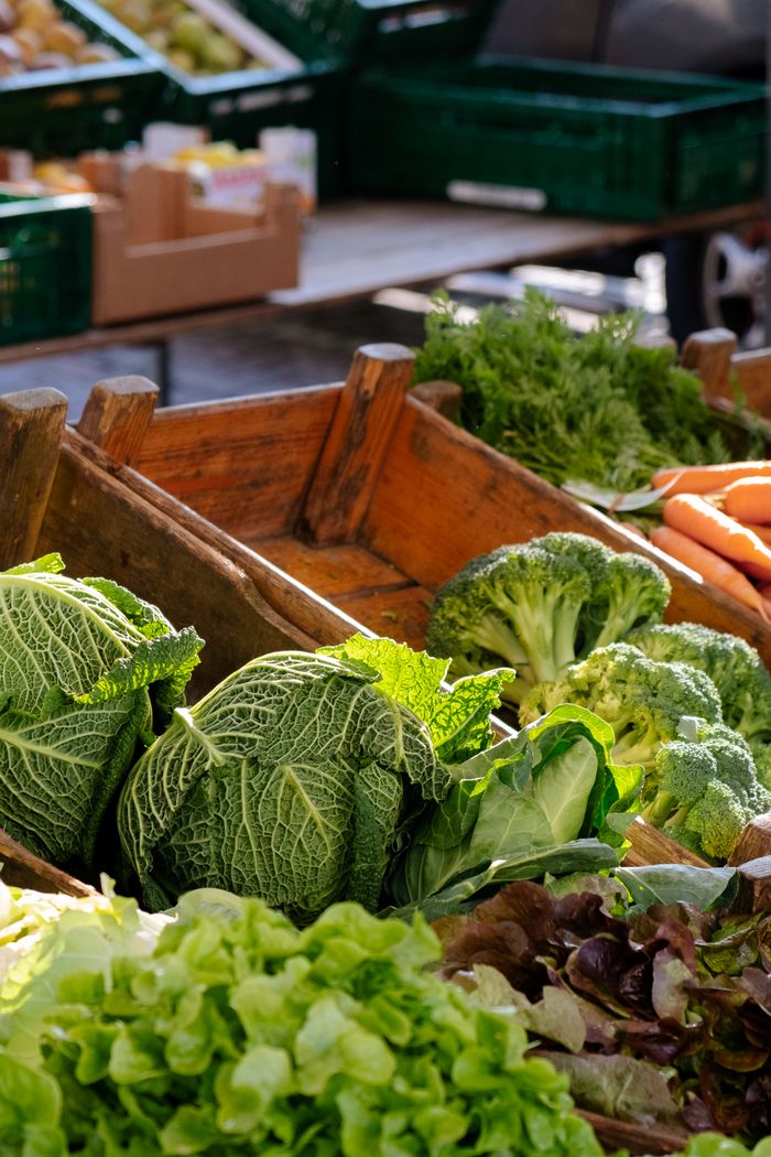 Home A vibrant display of fresh organic vegetables including cabbage, broccoli, and carrots at an outdoor market.