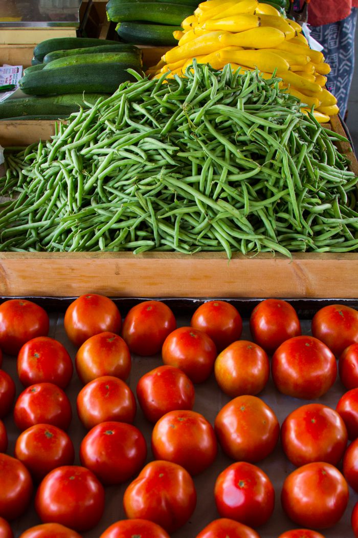 Home Fresh vegetables including green beans, tomatoes, zucchini, and squash neatly arranged at a market.