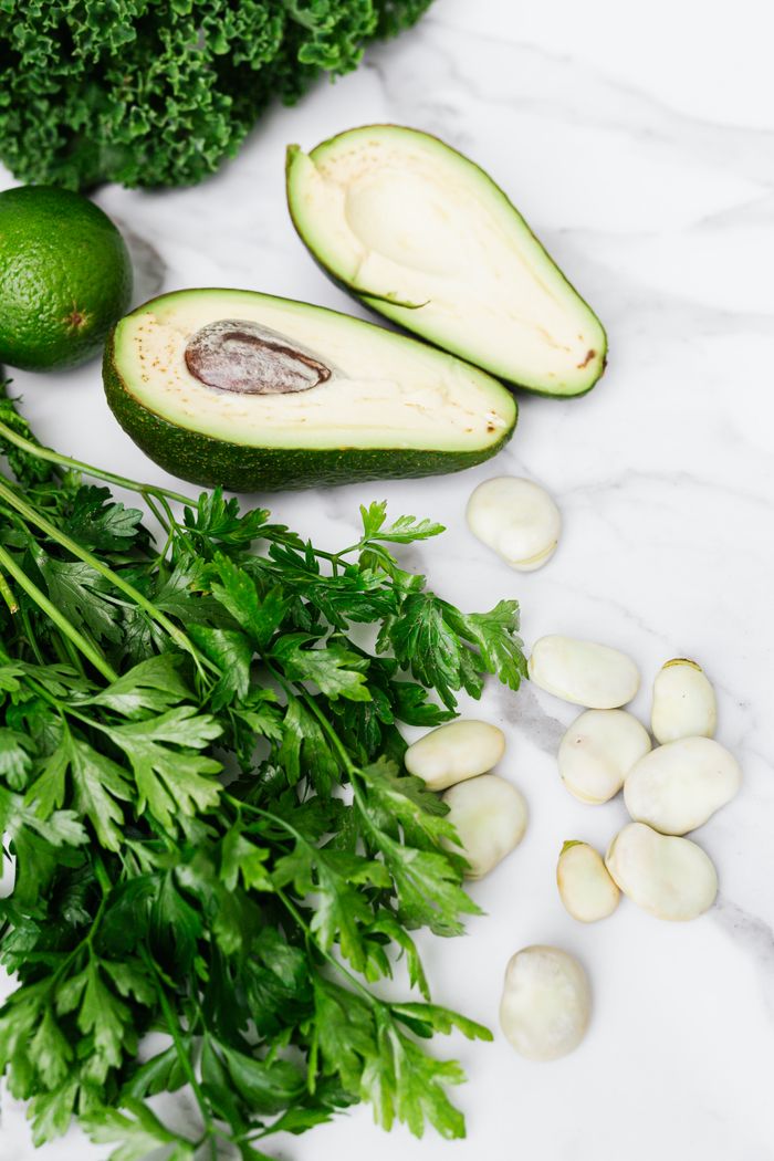 Home Crisp parsley, ripe avocado, broad beans, and lime on a white marble surface, a fresh culinary display.