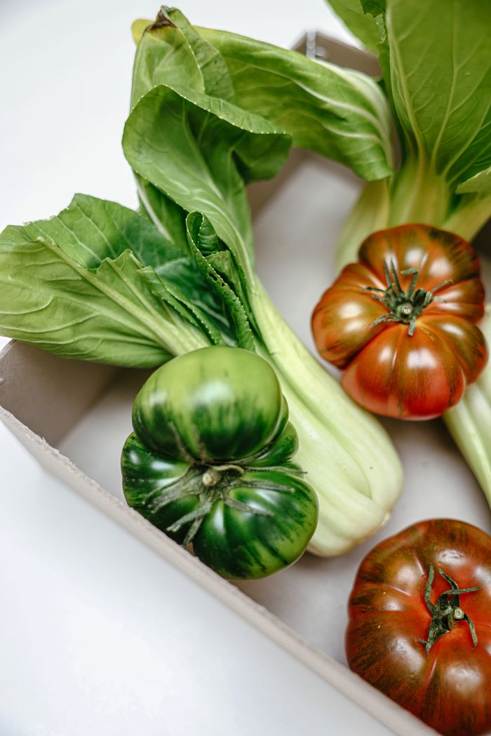 Home Close-up of fresh choy sum and heirloom tomatoes in a cardboard box, highlighting healthy eating.