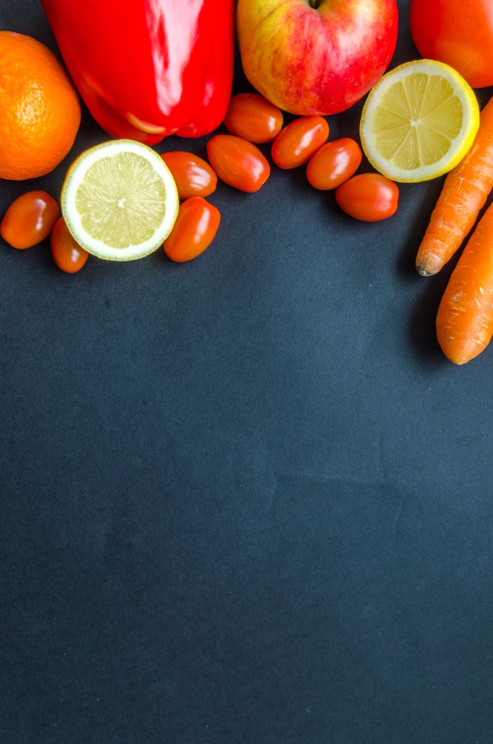 Home Colorful arrangement of fresh produce including citrus, carrots, and tomatoes on a dark backdrop.